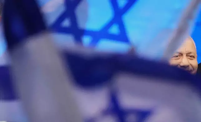 Gadi Eisenkot, leader of the Yashar party, is partially obscured by Israeli flags as he greets supporters after the release of the first exit poll results in Israel's general election in Tel Aviv, Israel, Tuesday, Oct. 27, 2026. (AP Photo/Ariel Schalit)