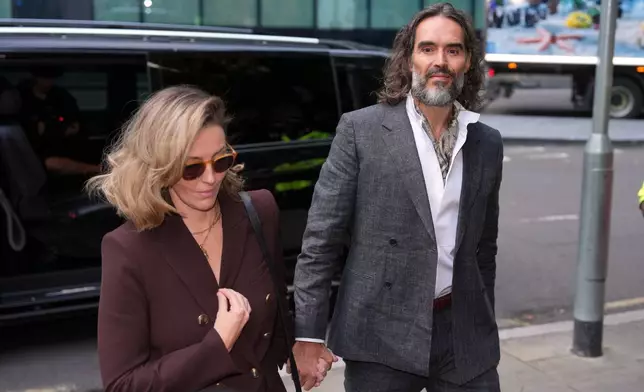 Comedian and actor Russell Brand, accompanied by his wife Laura Brand, arrives at Southwark Crown Court where he is charged with counts of rape and sexual assault against six women, which he has denied, in London, Monday, Oct. 12, 2026.(AP Photo/Kin Cheung)