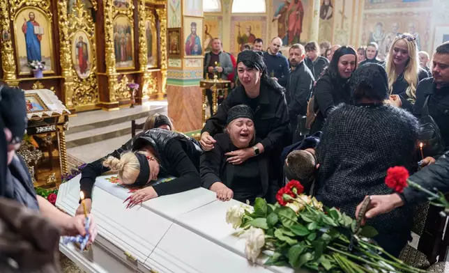 A mother surrounded by family cries sitting by the coffin of her son Illia Honcharenko, 14, killed by a Russian rocket strike on a residential house on Sept. 30, during their funeral, in Vyshhorod, Kyiv region, Ukraine, Friday, Oct. 2, 2026. (AP Photo/Evgeniy Maloletka)
