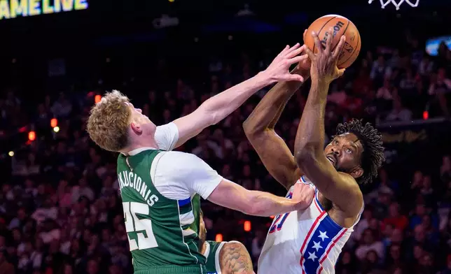 Philadelphia 76ers' Joel Embiid, right, goes up for the shot as he is fouled by Milwaukee Bucks' Kasparas Jakucionis, left, during the first half of an NBA basketball game, Saturday, Oct. 24, 2026, in Philadelphia. (AP Photo/Chris Szagola)