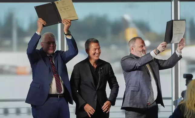 U.S. Transportation Secretary Sean Duffy, center, reacts while presenting the certification of Boeing's 737 Max 10 aircraft to Jim Williams, Boeing 737 Development Program chief engineer, at left, and Chris Payne, Boeing Commercial Airplanes vice president and program manager, 737 Development Programs, right, Tuesday, Oct. 20, 2026, at Boeing's factory in Everett, Wash. (AP Photo/Lindsey Wasson)