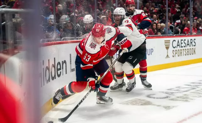 Washington Capitals left wing Ivan Miroshnichenko (63) and New Jersey Devils defenseman Dougie Hamilton (7) battle for the puck in the corner during the first period of an NHL hockey game against New Jersey Devils, Saturday, Oct. 17, 2026, in Washington. (AP Photo/Nathan Howard)