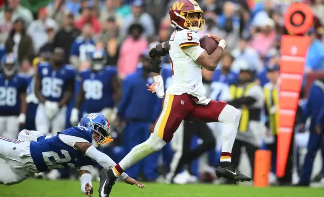 Washington Commanders quarterback Jayden Daniels (5) runs away from New York Giants cornerback Dru Phillips (22) for a touchdown during the second half of an NFL football game in Landover, Md., Sunday, Oct. 11, 2026. (AP Photo/Nick Wass)