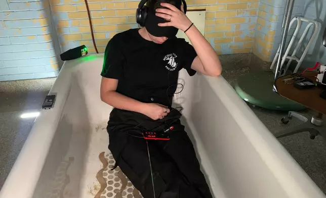 A blindfolded Ayla Robinson, a team manager with Michighost Paranormal, lies in a bathtub at Eloise Asylum during a paranormal investigation Monday, Oct. 12, 2026, in Westland, Mich. (AP Photo/Mike Householder)