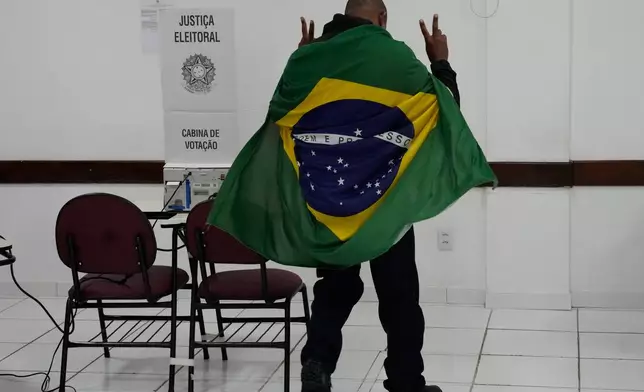 A man wrapped in a Brazilian flag arrives to vote in the presidential runoff in Brasilia, Brazil, Sunday, Oct. 25, 2026. (AP Photo/Eraldo Peres)