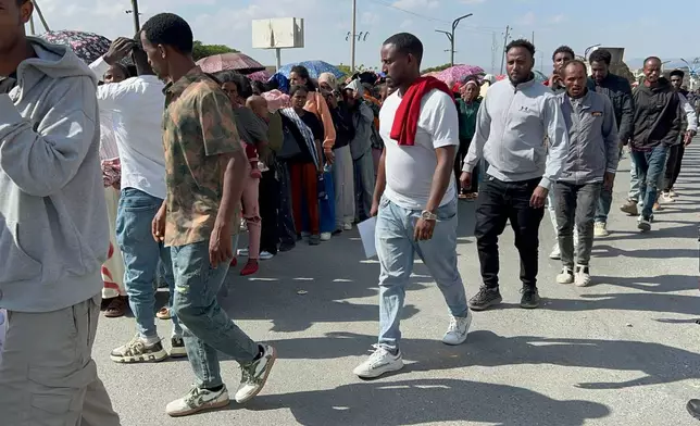 In this photo made with a smartphone, former Tigrayan fighters walk past people waiting under umbrellas as they line up for a disarmament, demobilization and reintegration program in Mekelle, Ethiopia, Thursday, Oct. 15, 2026. The program is intended to help former combatants return to civilian life. (AP Photo/Filmon Equar Hailu)