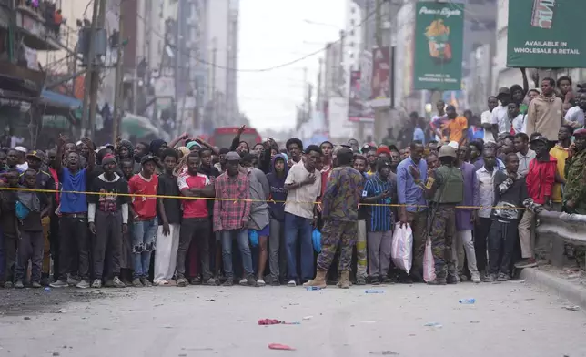 People watch from behind a security cordon after a multi-story building collapsed in Nairobi, Kenya, Friday, Oct. 23, 2026. (AP Photo/Brian Inganga)