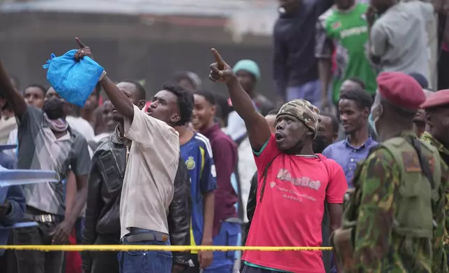 People watch from behind a security cordon after a multi-story building collapsed in Nairobi, Kenya, Friday, Oct. 23, 2026. (AP Photo/Brian Inganga)