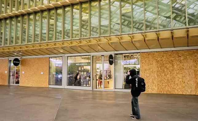 A man walks past stores boarded up with wooden planks in the Les Halles shopping district, which is under a nighttime curfew following weekend protests over the cost of living that turned into rioting and looting across France, in Paris, Wednesday, Oct. 21, 2026. (AP Photo/Teresa Suarez)