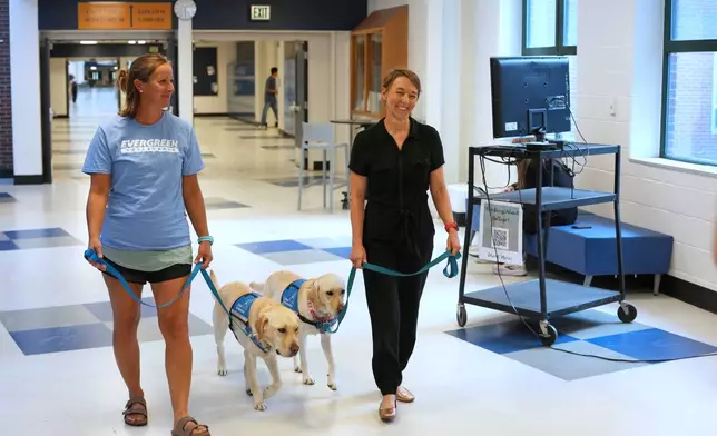 Amy Wells, left, counselor at Evergreen High School, walks with her support dog, Polenta, while talking with school principal Skyler Artes, who is leading her support dog, Noreen, through the halls of the school Monday, Oct. 5, 2026, in Evergreen, Colo. (AP Photo/David Zalubowski)