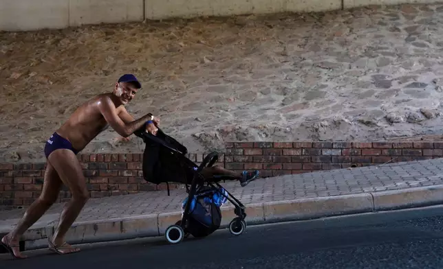 A father walks with a stroller and a baby on the streets wearing purple swim briefs during an event to raise awareness about prostate cancer, in Johannesburg, Friday, Oct. 23, 2026. (AP Photo)