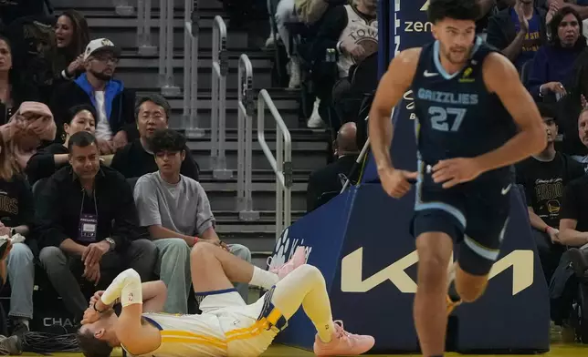 Golden State Warriors guard Brandin Podziemski, bottom, reacts on the floor as Memphis Grizzlies forward Cameron Boozer (27) runs up the court during the first half of an NBA basketball game, Friday, Oct. 23, 2026, in San Francisco. (AP Photo/Jeff Chiu)