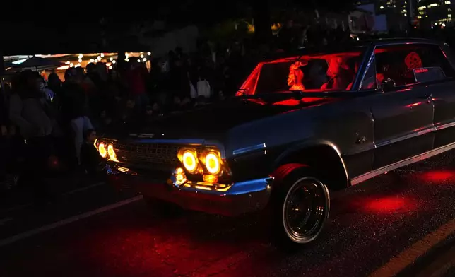 Marc Bautista and Cassandra Harrisson ride in their 1963 Chevy Impala during a Día de Muertos celebration and parade at Pike Place Market, Friday, Oct. 23, 2026, in Seattle. (AP Photo/Lindsey Wasson)