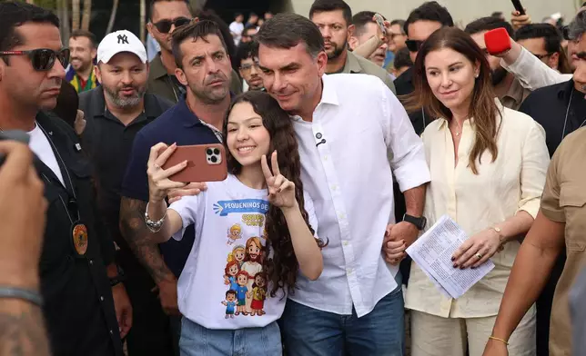 Opposition presidential candidate Sen. Flavio Bolsonaro, center, and his wife Fernanda pose for a selfie with a youth after attending Mass at the Metropolitan Cathedral of Our Lady of Aparecida, the patron saint of Brazil, on her feast day in Brasilia, Brazil, Monday, Oct. 12, 2026. (AP Photo/Arthur Menescal)