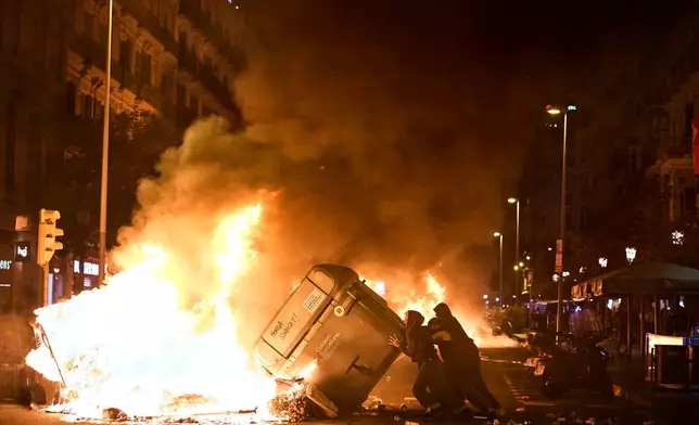Protesters set trash cans on fire during clashes with police following a demonstration over Spain's housing crisis, hours after Prime Minister Pedro Sánchez announced an early general election, in Barcelona, Spain, Monday, Oct. 5, 2026. (AP Photo/Emilio Morenatti)