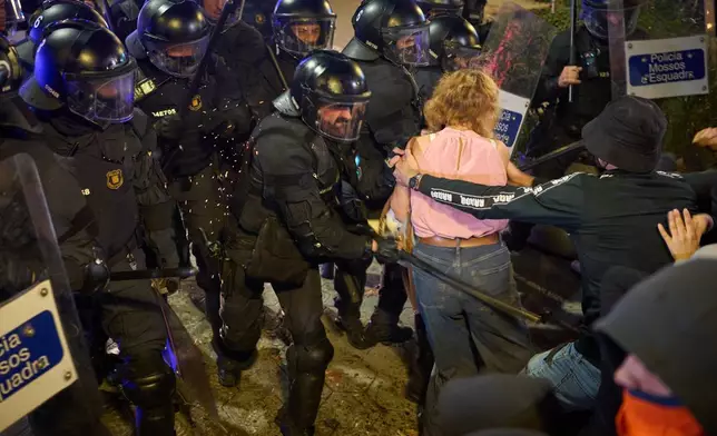 Riot police use their batons to disperse protesters following a demonstration over Spain's housing crisis, hours after Prime Minister Pedro Sánchez announced an early general election, in Barcelona, Spain, Monday, Oct. 5, 2026. (AP Photo/Emilio Morenatti)