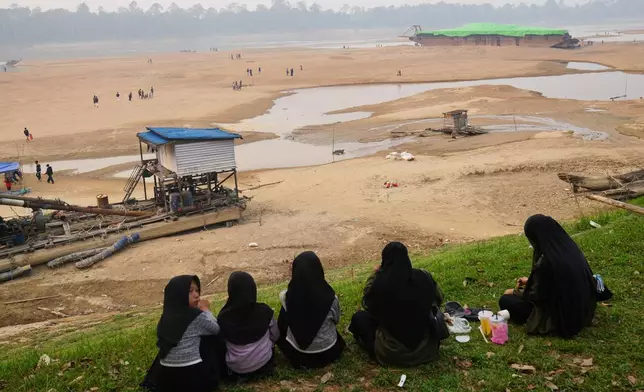People look at a barge, back right, stranded on a dry riverbed of the Kapuas River amid a drought in Sekadau, West Kalimantan, Indonesia, Friday, Sept. 11, 2026. (AP Photo/Tatan Syuflana)