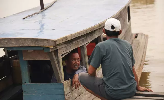 Abiansah, a boat operator, left, talks with a man at a wooden dock along the Kapuas River amid haze in Sekadau, West Kalimantan, Indonesia, Saturday, Sept. 12, 2026. (AP Photo/Tatan Syuflana)