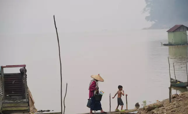A woman carrying buckets walks with a boy along the Kapuas River amid haze in Sanggau, West Kalimantan, Indonesia, Saturday, Sept. 12, 2026. (AP Photo/Tatan Syuflana)