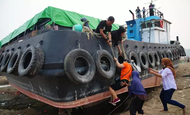A man helps a woman climb aboard a tugboat grounded on a riverbed of the Kapuas River amid a drought in Sekadau, West Kalimantan, Indonesia, Friday, Sept. 11, 2026. (AP Photo/Tatan Syuflana)