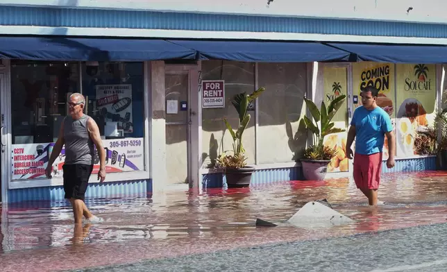 Pedestrians walk through a flooded street caused by king tides and heavy rain Wednesday, Oct. 28, 2026, in North Bay Village, Fla. (AP Photo/Marta Lavandier)