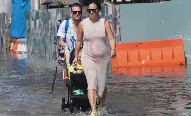 Pedestrians walk through a flooded street caused by king tides and heavy rain in North Bay Village, Fla., Wednesday, Oct. 28, 2026, (AP Photo/Marta Lavandier)