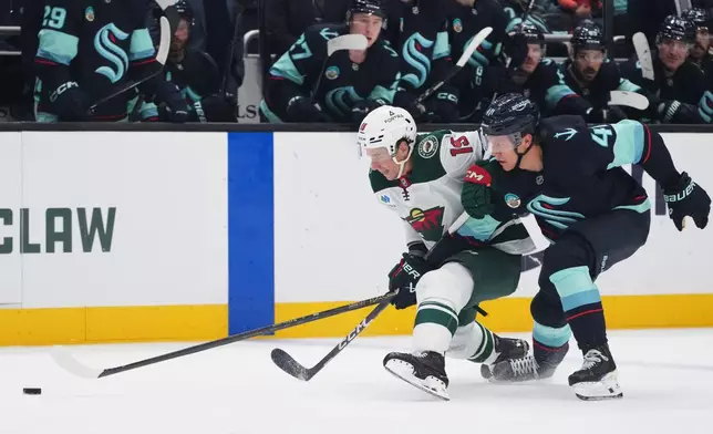 Minnesota Wild center Tyler Pitlick, left, and Seattle Kraken defenseman Ryker Evans, right, grapple for position as they chase the puck during the third period of an NHL hockey game Saturday, Oct. 24, 2026, in Seattle. (AP Photo/Lindsey Wasson)