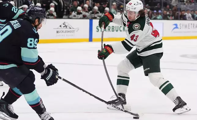 Seattle Kraken center Frederick Gaudreau (89) blocks a shot from Minnesota Wild defenseman Quinn Hughes (43) during the first period of an NHL hockey game Saturday, Oct. 24, 2026, in Seattle. (AP Photo/Lindsey Wasson)