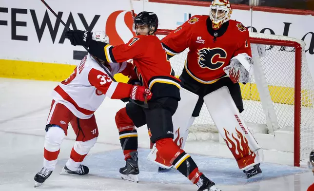 Detroit Red Wings' Viktor Arvidsson, left, is checked by Calgary Flames' Kevin Bahl, center, as goalie Devin Cooley follows the play during the first period of an NHL hockey game in Calgary, Alberta, Saturday, Oct. 24, 2026.(Jeff McIntosh/The Canadian Press via AP)