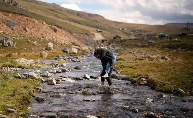A man carries a woman on his back across a stream to reach the rock where Trabzonspor's Egyptian soccer player Mohamed Salah previously posed for a photo he shared on social media, in Trabzon province, along Turkey's Black Sea coast, Monday, Oct. 19, 2026. (AP Photo/Khalil Hamra)