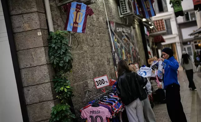 Women shop for soccer jerseys at a street stall displaying a Trabzonspor jersey bearing the name of the club's Egyptian player Mohamed Salah in Trabzon, Turkey, Monday, Oct. 19, 2026. (AP Photo/Khalil Hamra)