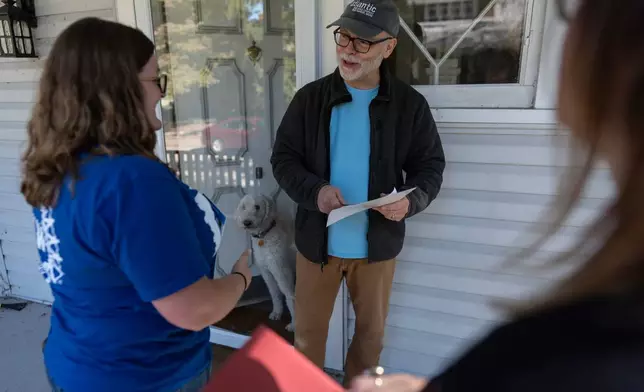 Morgan Hughes, left, and Jordan "JoJo" Burkhard, right, both members of UAW Local 402, in Springfield, Ohio, talks with Barry Milligan, center, as his dog Lorna, looks out form the doorway, as Jughes and Burkhard canvas for votes in Kettering, Ohio, Monday, Sept. 28, 2026. (AP Photo/Carolyn Kaster)