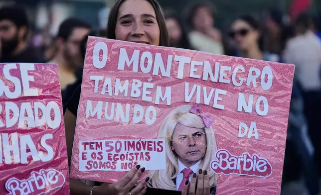 A woman holds a banner referring to Portugal’s Prime Minister Luis Montenegro during a protest to demand affordable housing in Lisbon on Saturday, Oct. 24, 2026. The test reads in Portuguese: "Montenegro also lives in Barbie world. He owns 50 properties, yet we're the selfish ones.". (AP Photo/Ana Brigida)