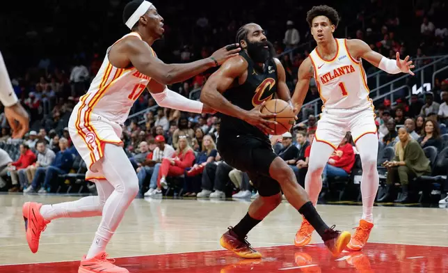 Cleveland Cavaliers guard James Harden, center, drives against Atlanta Hawks forwards Onyeka Okongwu (17) and Jalen Johnson (1) during the first half of an NBA basketball game, Thursday, Oct. 29, 2026, in Atlanta. (AP Photo/Erik S. Lesser)