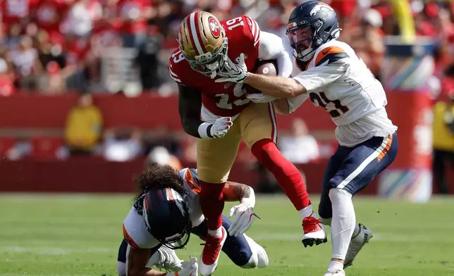 San Francisco 49ers wide receiver Deebo Samuel Sr., middle, runs against Denver Broncos safety Talanoa Hufanga, bottom, and cornerback Riley Moss (21) during the first half of an NFL football game in Santa Clara, Calif., Sunday, Oct. 4, 2026. (AP Photo/Kelley L. Cox)