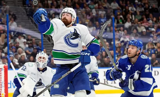 Vancouver Canucks defenseman Filip Hronek (17) bats the puck away from Tampa Bay Lightning center Brayden Point (21) during the second period of an NHL hockey game Saturday, Oct. 17, 2026, in Tampa, Fla. (AP Photo/Chris O'Meara)