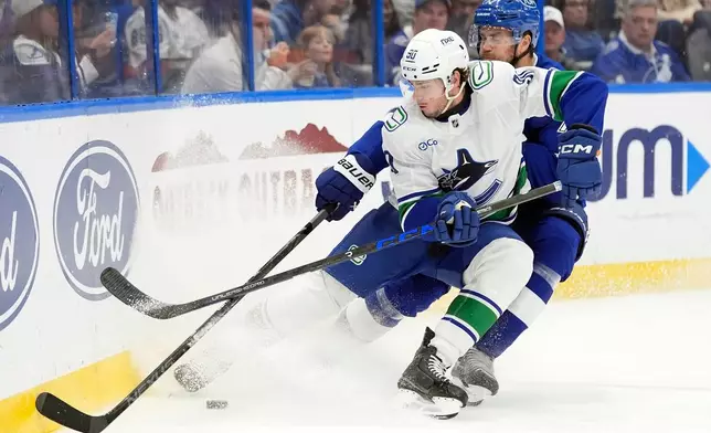 Vancouver Canucks defenseman Victor Mancini (90) beats Tampa Bay Lightning defenseman Victor Hedman (77) to a loose puck during the second period of an NHL hockey game Saturday, Oct. 17, 2026, in Tampa, Fla. (AP Photo/Chris O'Meara)