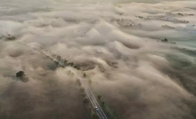 A car is seen driving on a road through foggy landscape in the Taunus region near Frankfurt, Germany, Friday, Oct. 2, 2026. (AP Photo/Michael Probst)