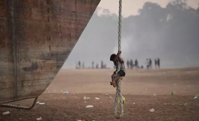 A boy climbs a rope hanging from a barge stranded on a dry riverbed of the Kapuas River amid a drought in Sekadau, West Kalimantan, Indonesia, Friday, Sept. 11, 2026. (AP Photo/Tatan Syuflana)