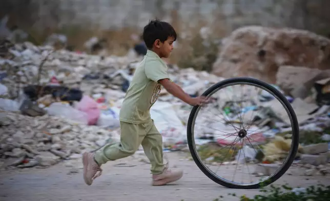 A boy rolls a bicycle wheel past rubble as he plays in a neighborhood damaged during the civil war in Homs, Syria, Thursday, Oct. 1, 2026. (AP Photo/Ghaith Alsayed)