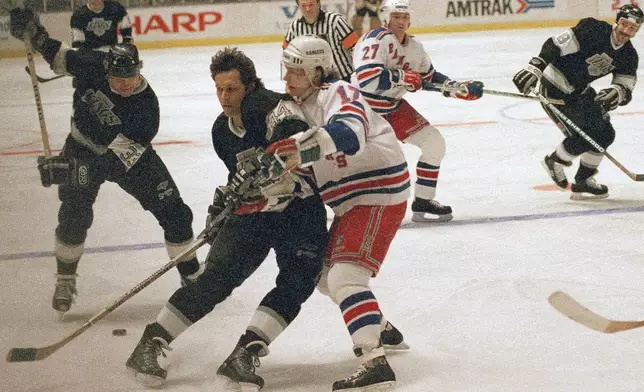 FILE - Marty McSorley, left, of the Los Angeles Kings winds up before shooting the puck as teammate Ron Duguay, center, blocks out New York Rangers Carey Wilson during the first period of their National Hockey League game on Monday, Feb. 27, 1989 in New York. (AP Photo/Ron Frehm, File)