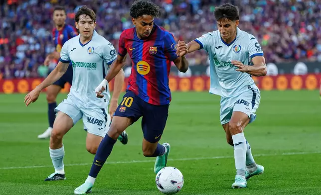 Barcelona's Lamine Yamal, centre, challenges for the ball with Getafe's Ramon Terrats, right, during the Spanish La Liga soccer match between Barcelona and Getafe in Barcelona, Spain, Saturday, Oct. 10, 2026. (AP Photo/Joan Monfort)