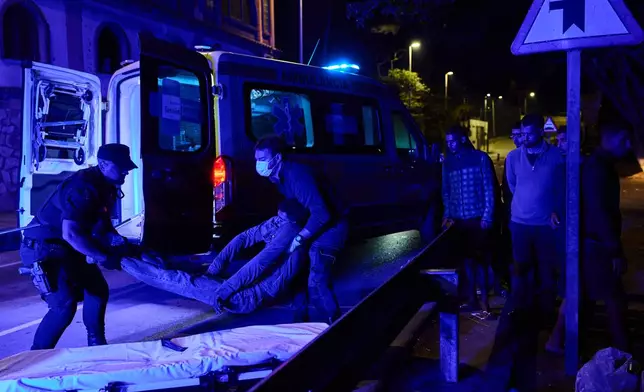 A police officer and a medical worker place a migrant who is unconscious following a fight with another group of migrants onto a stretcher to be taken to hospital on El Trampolín Beach in the Spanish enclave of Ceuta, Friday, Oct. 2, 2026. (AP Photo/Bernat Armangue)
