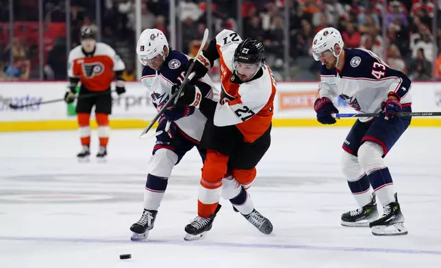 Philadelphia Flyers' Noah Cates, center, and Columbus Blue Jackets' Adam Fantilli (19) battle for the puck during the second period of an NHL hockey game, Tuesday, Oct. 27, 2026, in Philadelphia. (AP Photo/Derik Hamilton)