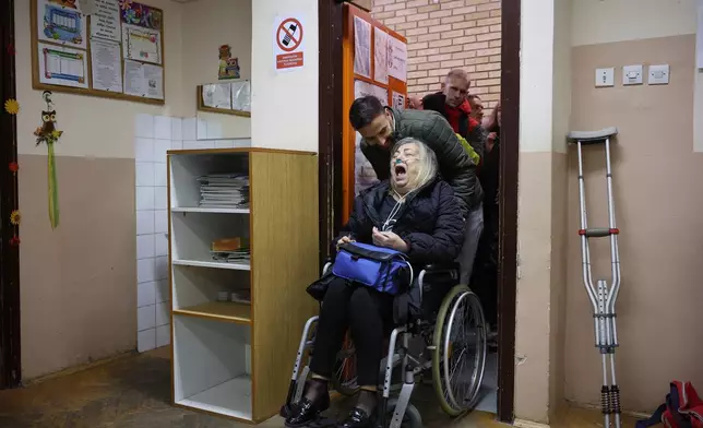 A wheelchair using woman shares a laugh with a man assisting her to vote at polling station that just opened its doors in a parliamentary election in Novi Sad, Serbia, Sunday, Oct. 25, 2026. (AP Photo/Armin Durgut)