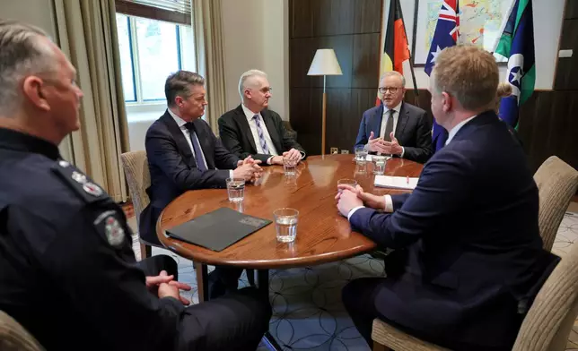 Australian Prime Minister Anthony Albanese, second right, Home Affairs Minister Tony Burke, third left, Victorian Premier Ben Carroll, Chief Commissioner of Victoria Police Mike Bush, left, Australian Federal Police Commissioner Krissy Barrett, obscured, and Victorian Police Minister Paul Edbrooke, right, hold a meeting following the attack on federal independent member of parliament, Helen Haines in Wangaratta, at the Commonwealth Offices in Melbourne, Australia, Tuesday, Oct. 20, 2026. (Con Chronis/AAP Image via AP)