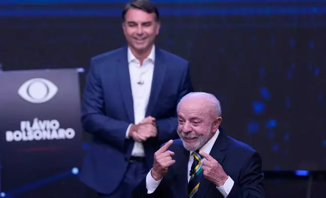 Brazilian President Luiz Inacio Lula da Silva, front, who is running for reelection, gestures toward his face as opposition presidential candidate Sen. Flavio Bolsonaro stands behind him during a televised presidential debate one week before the presidential runoff election in Sao Paulo, Brazil, Sunday, Oct. 18, 2026. (AP Photo/Andre Penner)