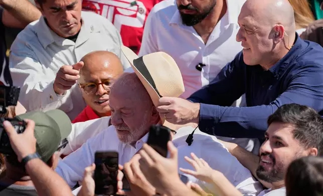 A security officer places a hat on President Luiz Inacio Lula da Silva as he leaves after voting during general elections amid a crowd in Sao Bernardo do Campo, Brazil, Sunday, Oct. 4, 2026. (AP Photo/Andre Penner)