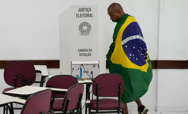 A voter wrapped in a Brazilian flag walks to an electronic voting machine to cast his ballot during general elections in Brasilia, Brazil, Sunday, Oct. 4, 2026. (AP Photo/Eraldo Peres)