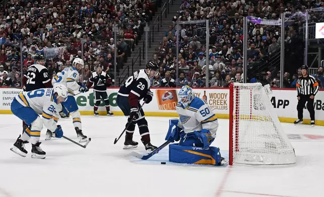 St. Louis Blues goaltender Jordan Binnington (50), right, stops a shot by Colorado Avalanche center Nathan MacKinnon (29), second from right, during the first period of an NHL hockey game Saturday, Oct. 3, 2026, in Denver. (AP Photo/RJ Sangosti)